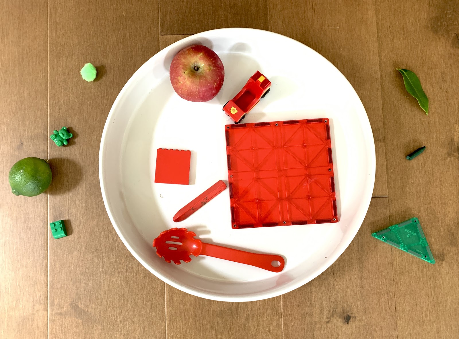 Un plato blanco con un número de objetos rojos en él; hay objetos verdes fuera del plato.