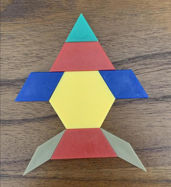 Pattern blocks in the shape of a rocket ship. The top is a triangle on top of a trapezoid. The body is a hexagon with 2 rhombus wings. The bottom is a trapezoid with two narrow rhombus tail pieces.