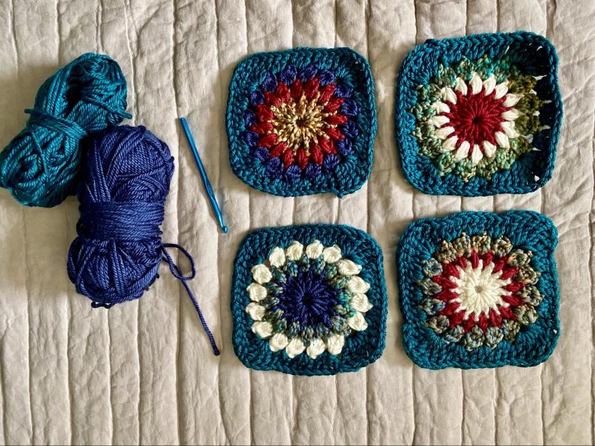 El dibujo muestra 2 ovillos de lana y una aguja de crochet. También muestra 2 filas de cuadrados tejidos que Jasmine hizo. Cada fila tiene 2 cuadrados. Cada cuadrado tiene 4 colores. El color de la orilla es igual para todos, pero los colores de adentro cambian.