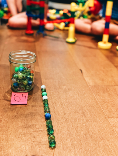 Looking from the front at the jar of marbles and the line of marbles next to the jar. From this angle, the marbles in a line are hard to count. We can also see one of Hayden and Charlotte's tracks in the background.
