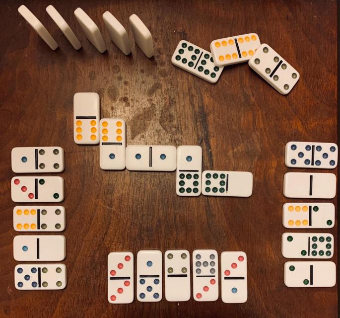5 groups of 5 dominoes + 1 group of 3. In 1 group, the dominoes stand up. In 4 groups, the dominoes are faceup. The group on the left has 3 dominoes that show 4 purple dots on one side. The group at the bottom has a double 3 domino. The group on the right has a double 0 domino. The dots in each of these groups total 30. The group in the middle is a domino train that links matching dot patterns. The dots in this group total 32. The group of 3 dominoes are all doubles.