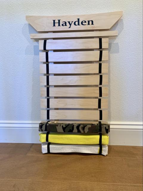 A belt rack from Taekwando class. The rack has space for 10 colors of belts. Starting at the bottom, Hayden has earned a white belt, a yellow belt, and a camouflage belt.