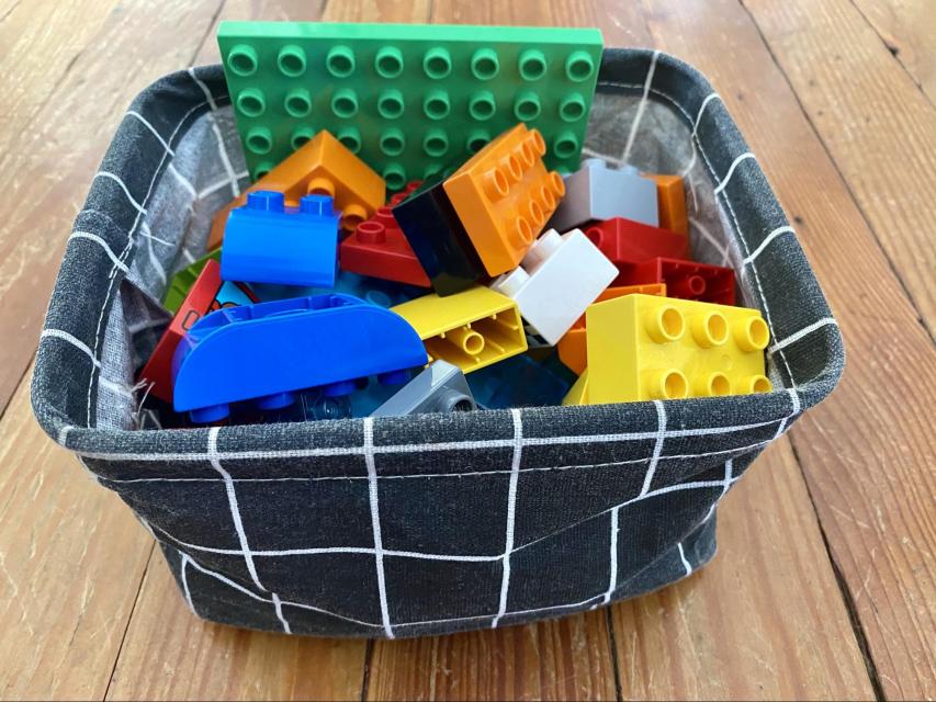 A fabric basket filled with assorted building blocks.