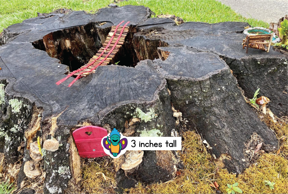 A tree stump has a small red door tucked into a crevice. It looks like the door opens into the stump. The fairy is next to the door. There's a big hole in the stump, but there's a bridge across it. The bridge is made from short sticks and red string. There's also a small chair made from the same kind of sticks.